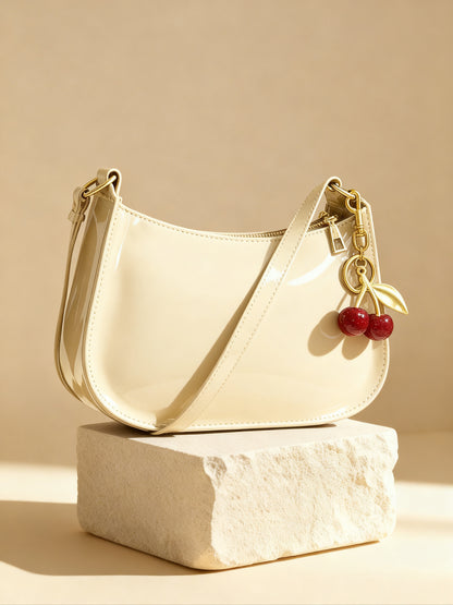 Cream vegan glossy handbag with cherry charm and shoulder strap on stone pedestal