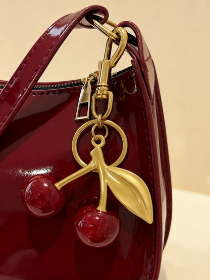 Close-up of gold-finish cherry charm on glossy patent bag in cherry red