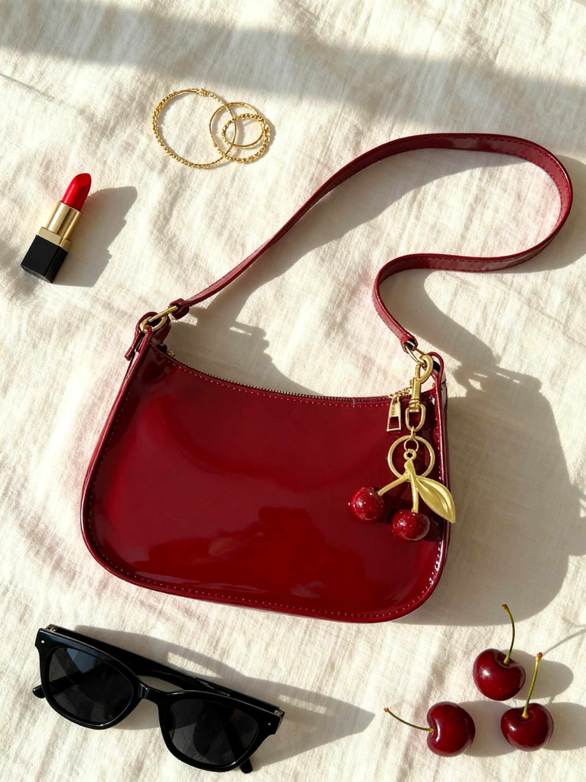 Red patent bag flat lay with sunglasses, lip gloss and fresh cherries - 90s shoulder bag