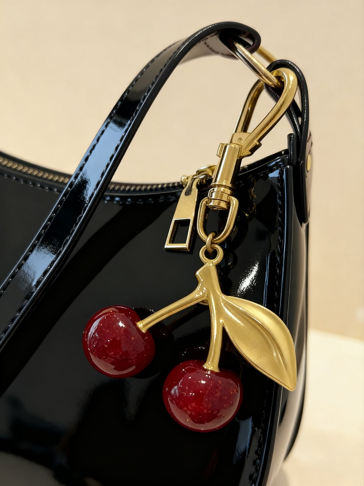 Close-up of gold-finish cherry charm on black vegan baguette bag