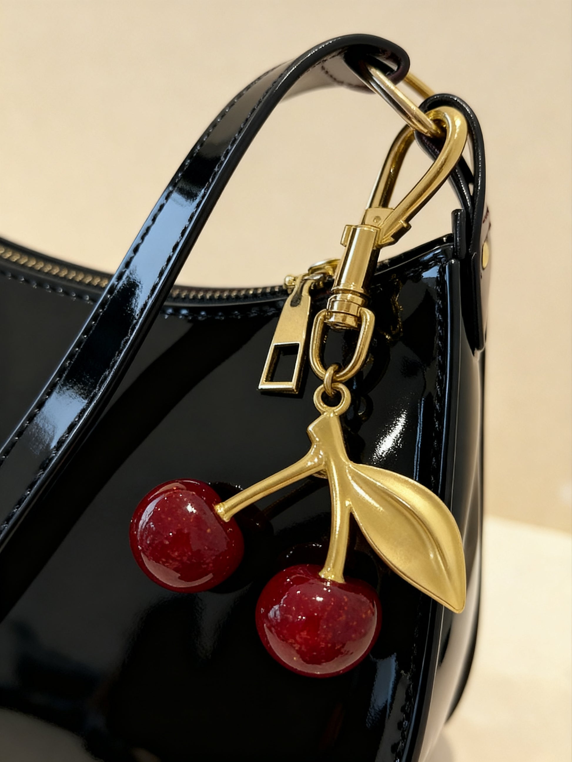 Close-up of gold-finish cherry charm on black vegan baguette bag